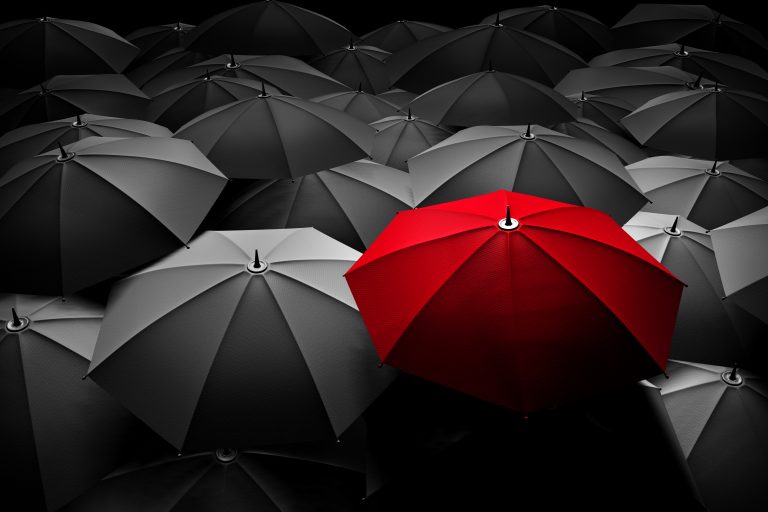 One red umbrella in a sea of grey umbrellas